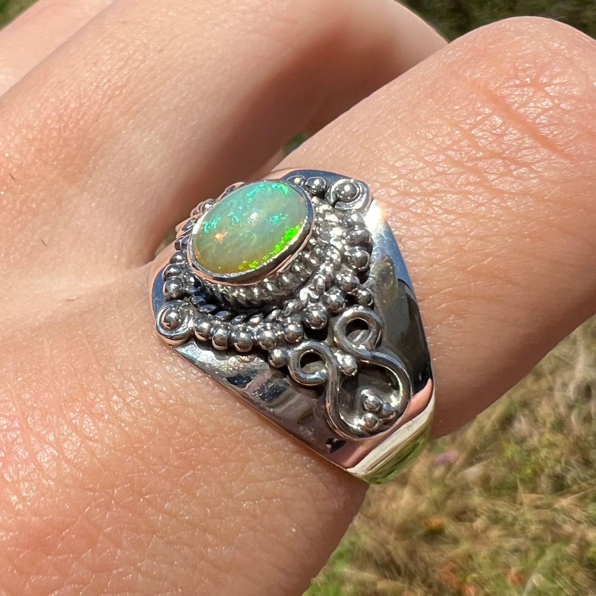 An Ethoipian opal boho ring shown at a macro angle, worn on a finger in sunlight.