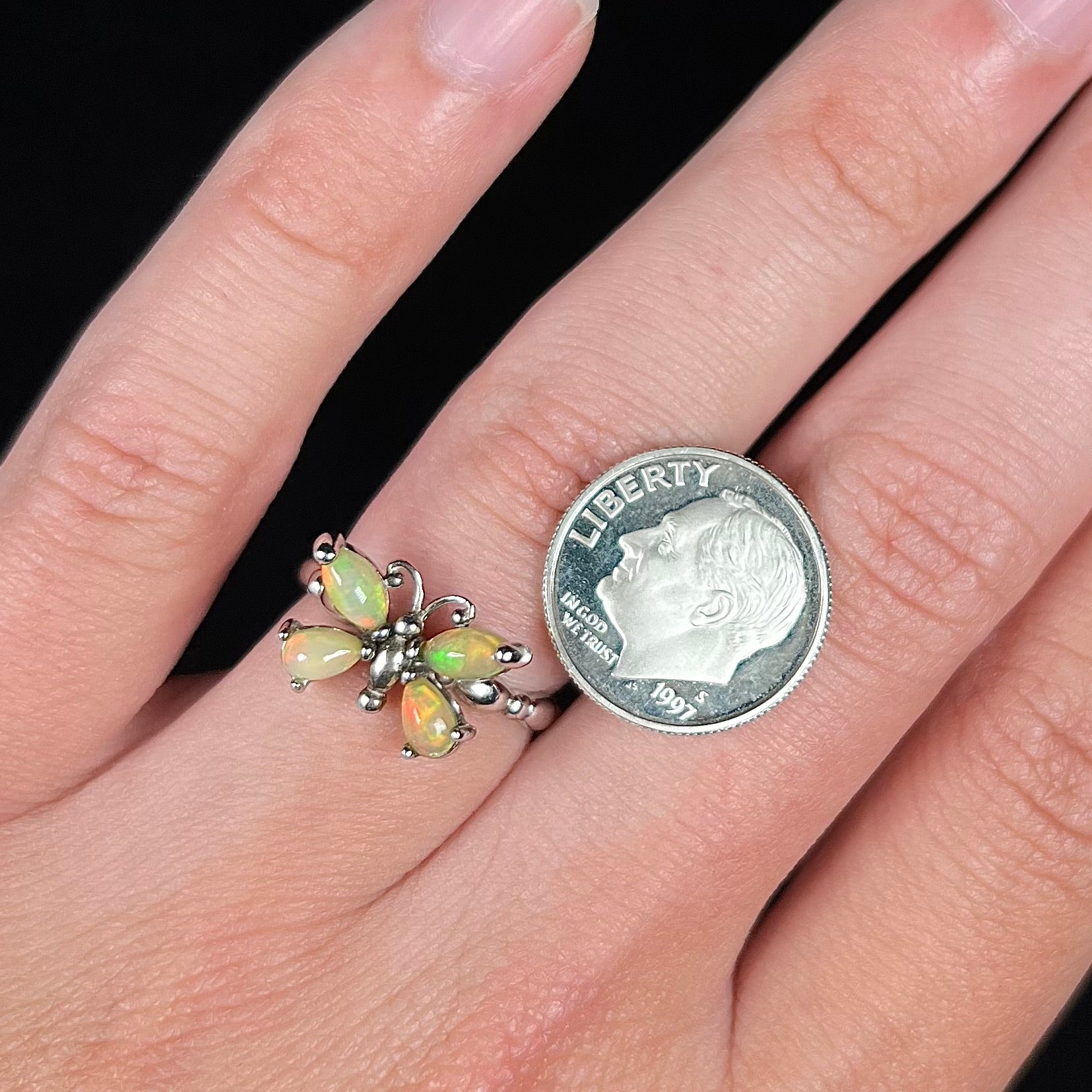 Close-up view of a sterling silver Ethiopian opal butterfly ring worn on a finger next to a dime coin.