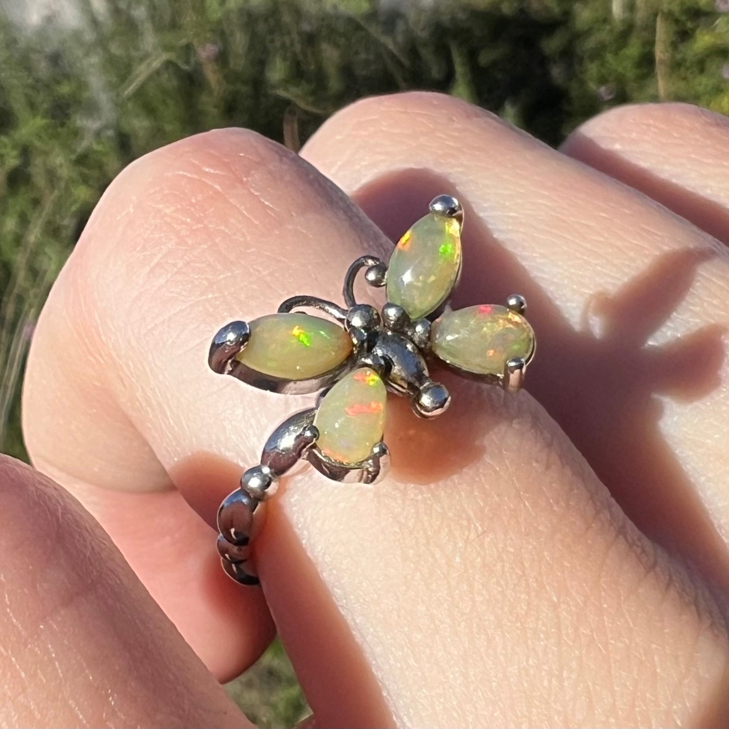 A sterling silver Ethiopian opal butterfly ring shown close-up in sunlight at an angle on a finger.