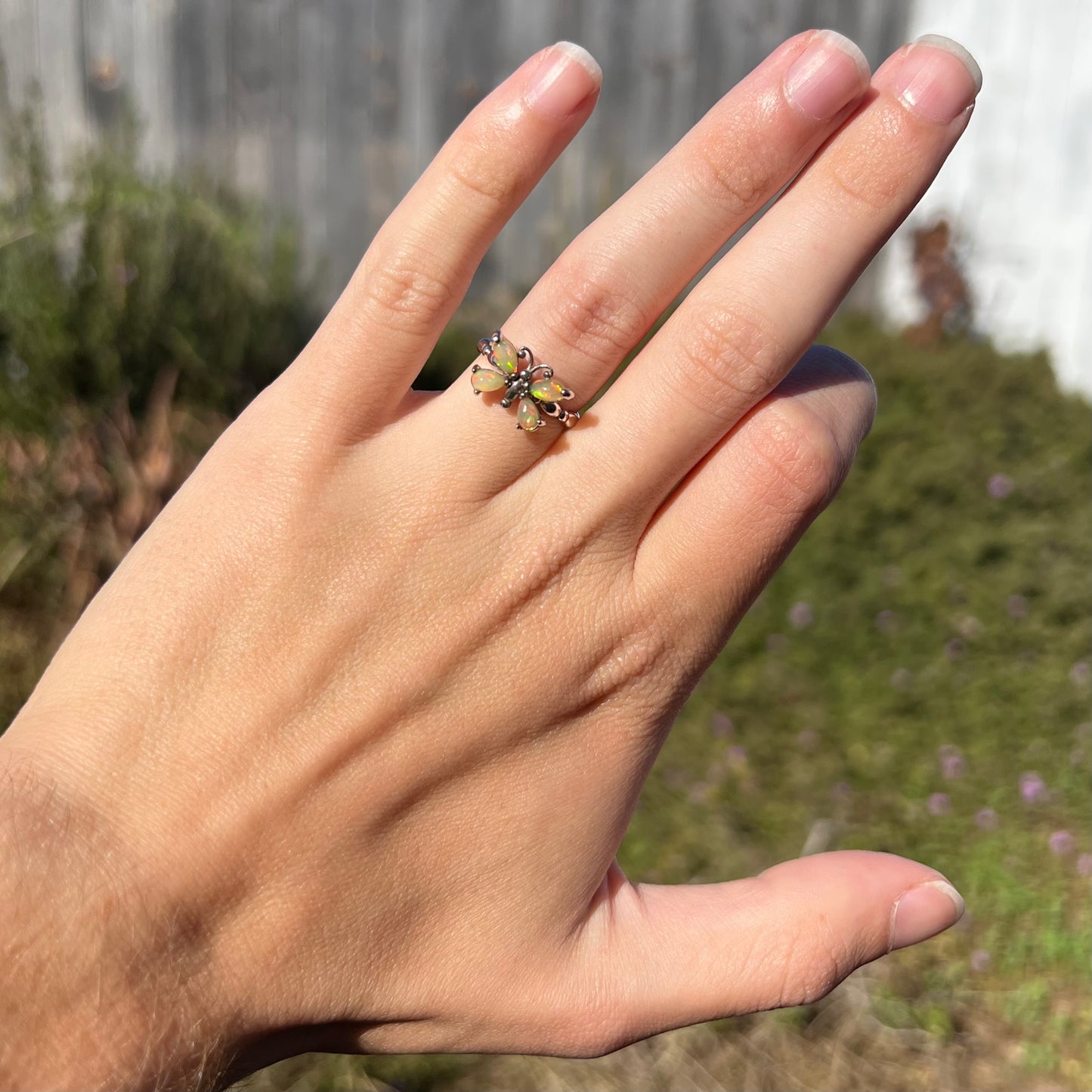 A sterling silver Ethiopian opal butterfly ring worn on a hand in sunlight against an outdoor background.