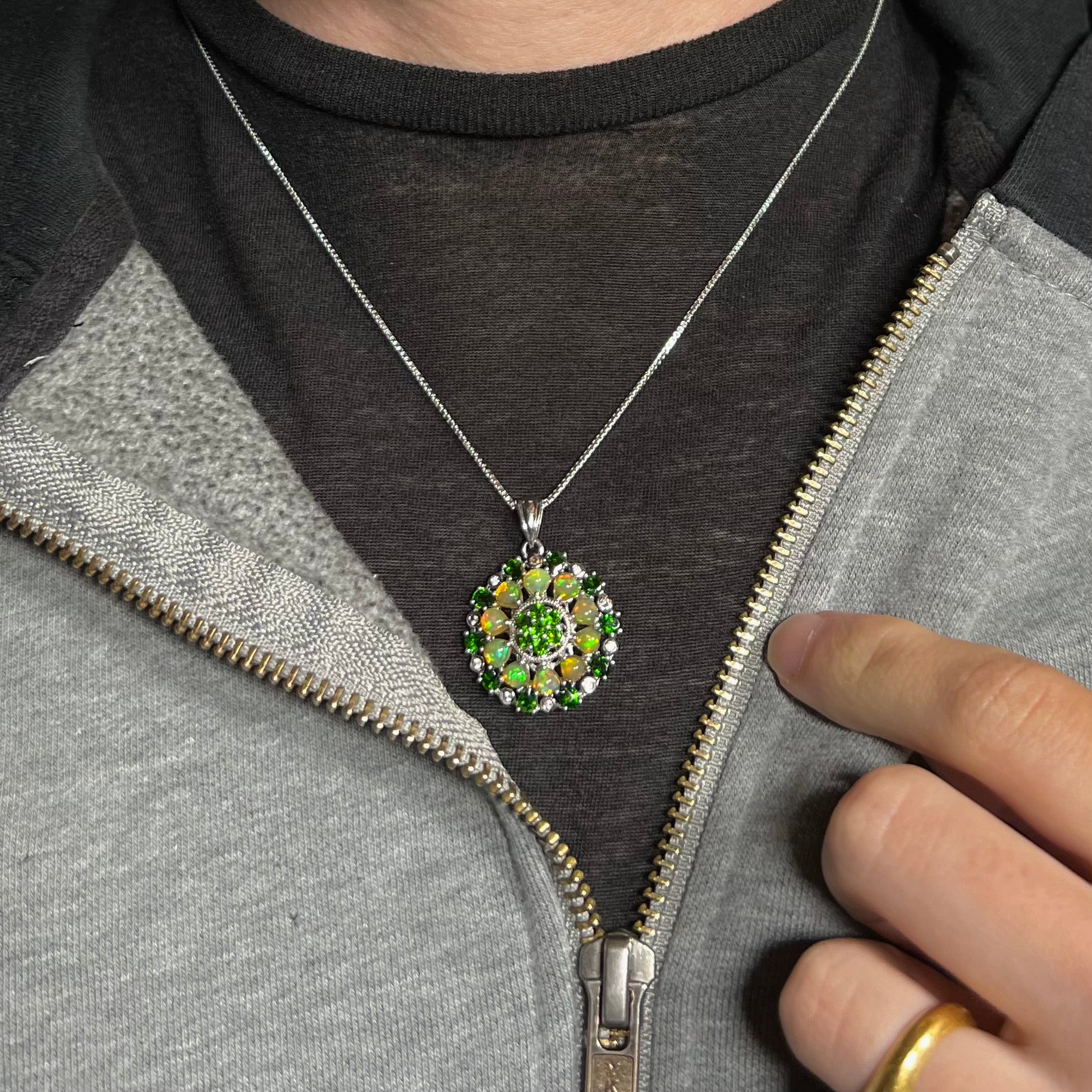 A silver Ethiopian opal and chrome diopside necklace worn against a dark shirt under an unzipped hoodie.