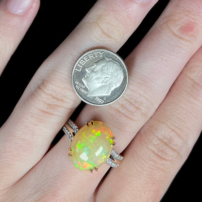 Close-up of hand wearing Ethiopian opal and diamond cocktail ring next to US dime coin for scale; the two are comparable in size