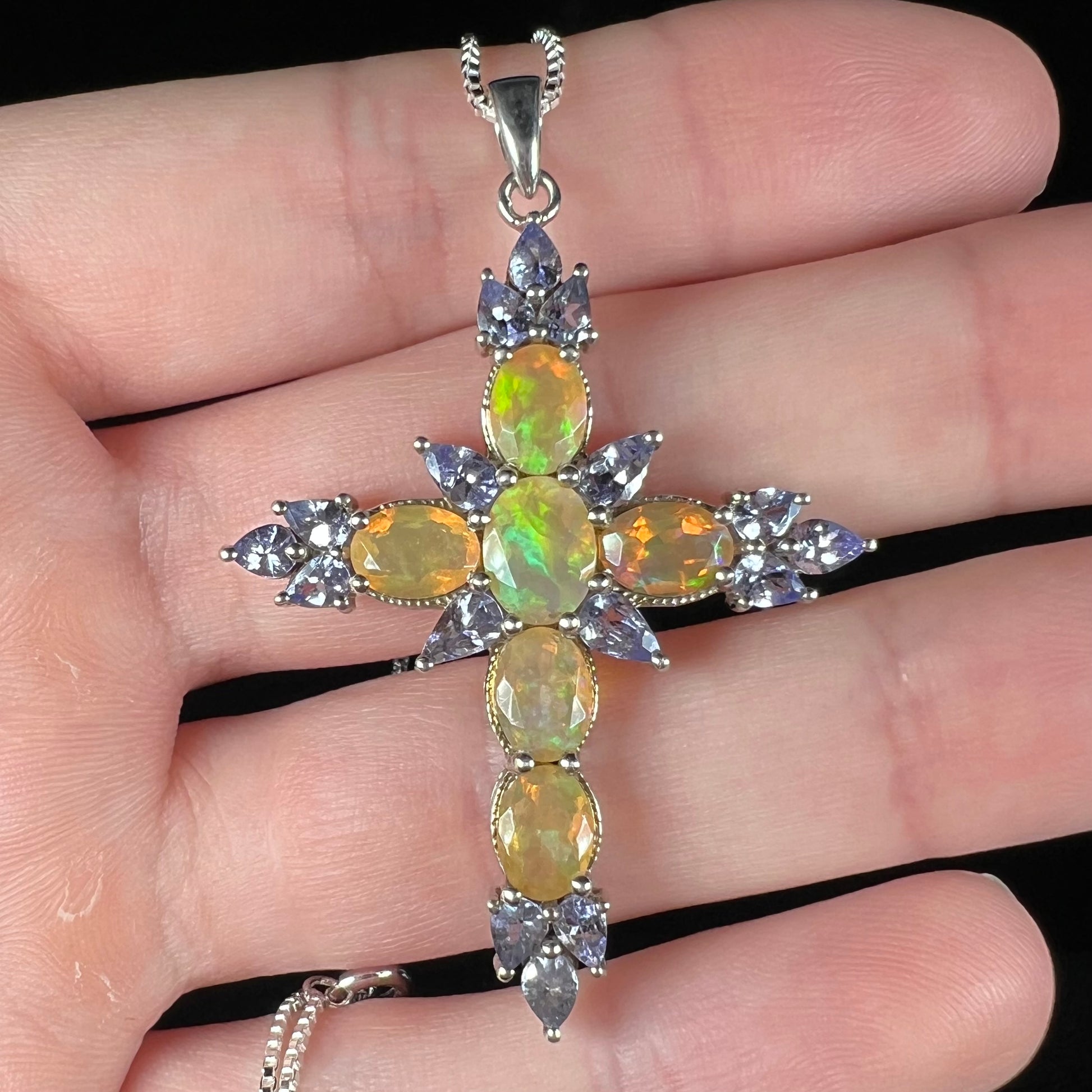 An Ethiopian opal and tananite cross pendant made from sterling silver, held in a hand showing the front.