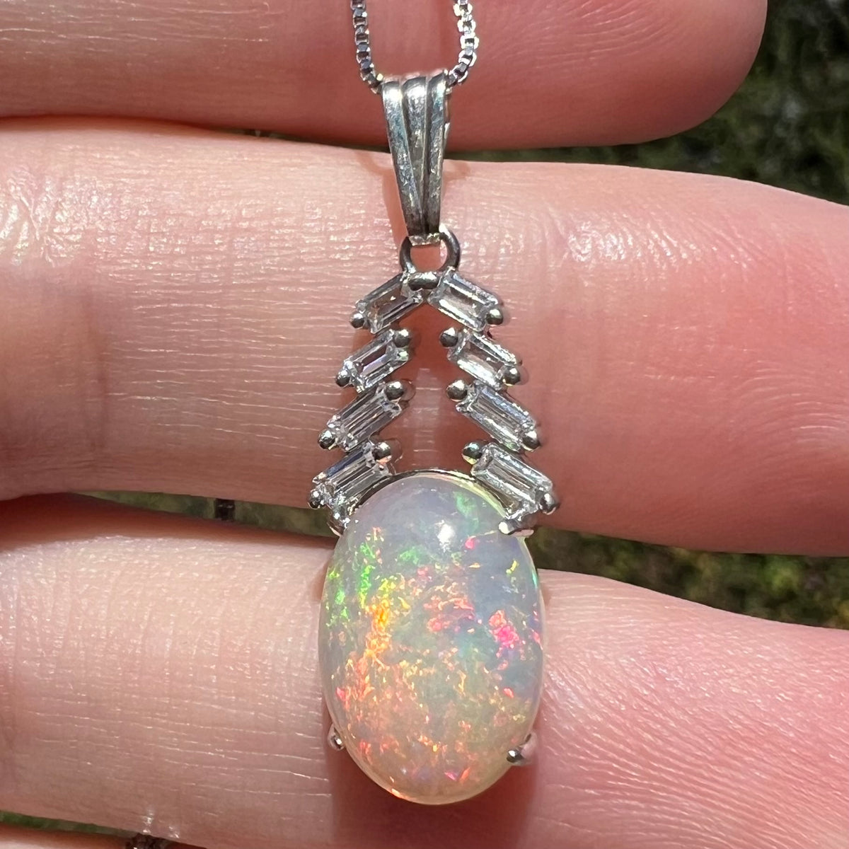 Close-up of women's silver Ethiopian opal and CZ drop pendant held in natural light