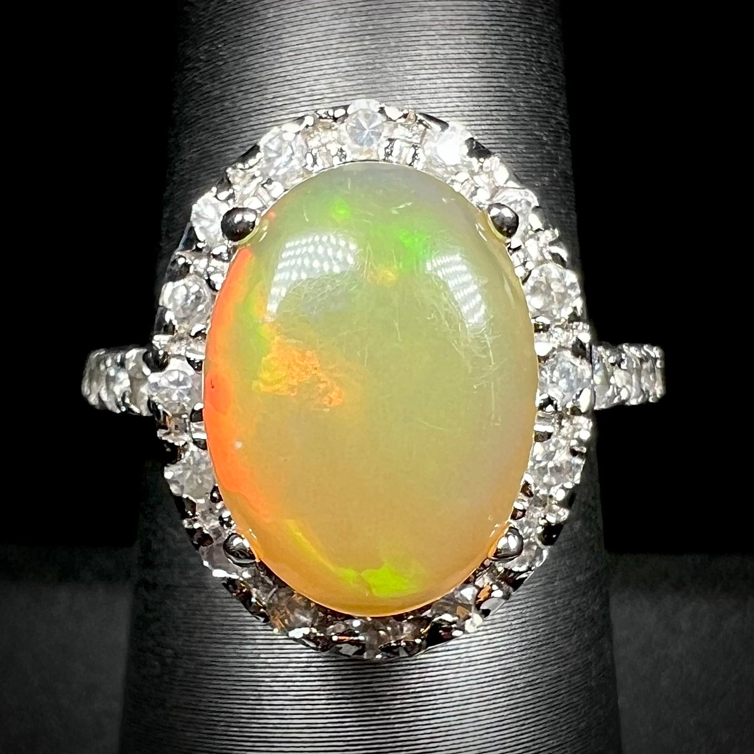 A sterling silver Ethiopian fire opal ring with a CZ halo shown from the front against a black backdrop.
