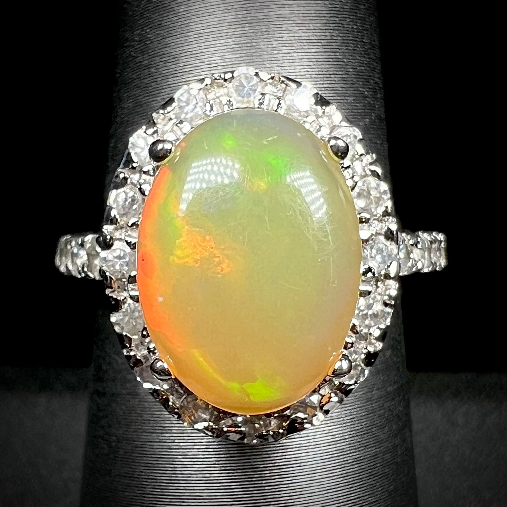 A sterling silver Ethiopian fire opal ring with a CZ halo shown from the front against a black backdrop.