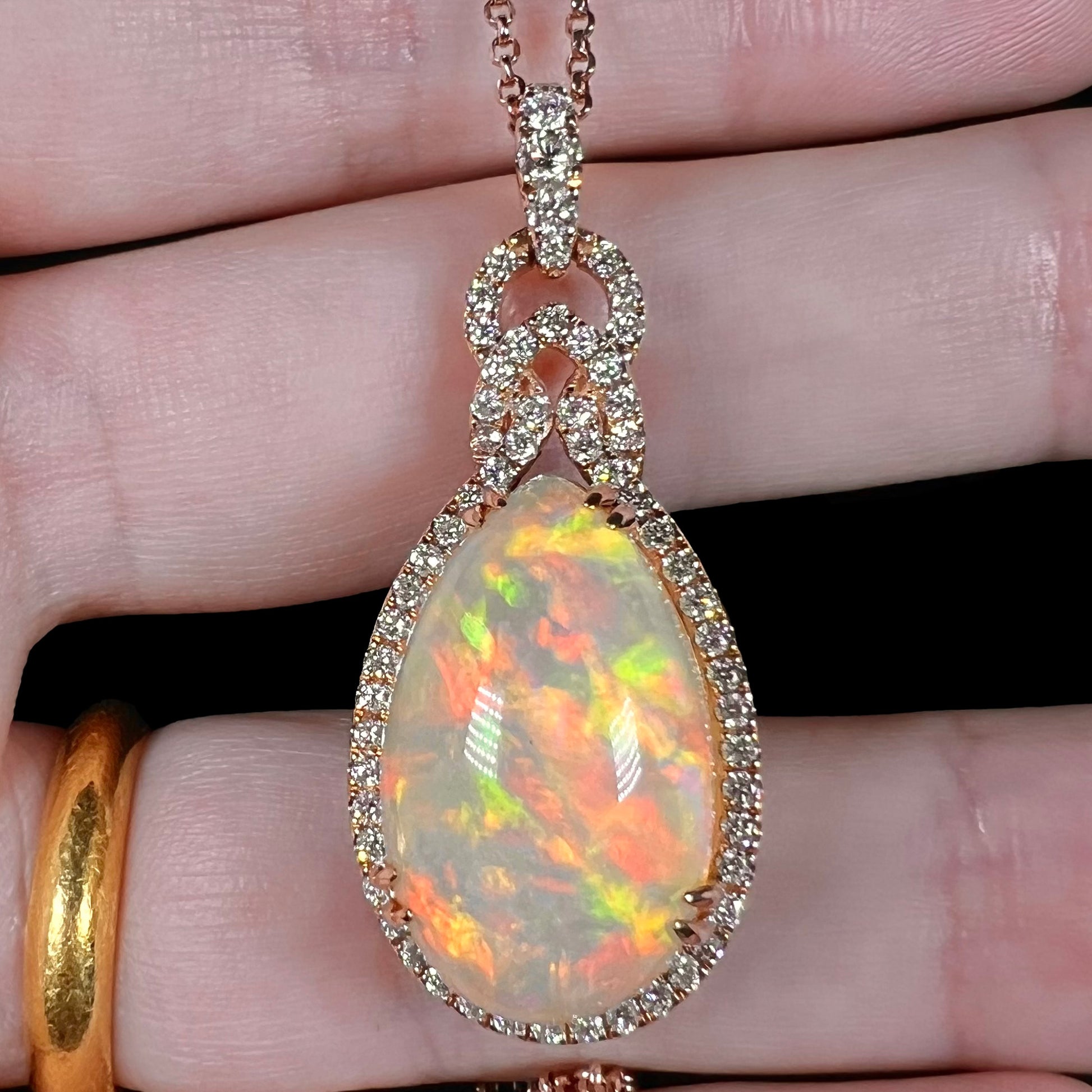 Close-up front view of an Ethiopian opal and diamond halo necklace by Le Vian shown held in a hand under LED studio lightning.