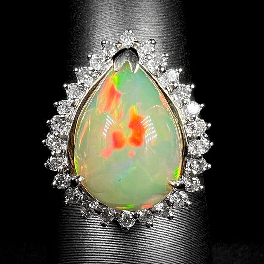 Front macro view of 18k white gold pear shaped Ethiopian opal and diamond halo ring with red flashes, shown on ring display.