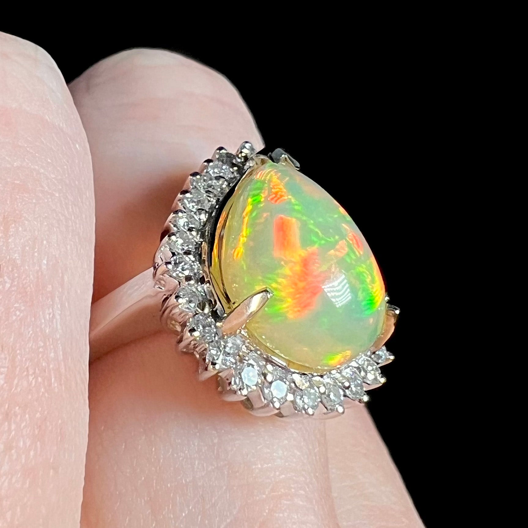 Red and green Ethiopian opal and diamond halo ring shown close-up on a finger from an angle.