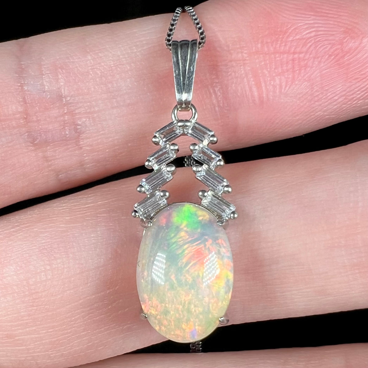 Macro close-up of oval shaped Ethiopian opal and emerald cut CZ pendant, held in hand