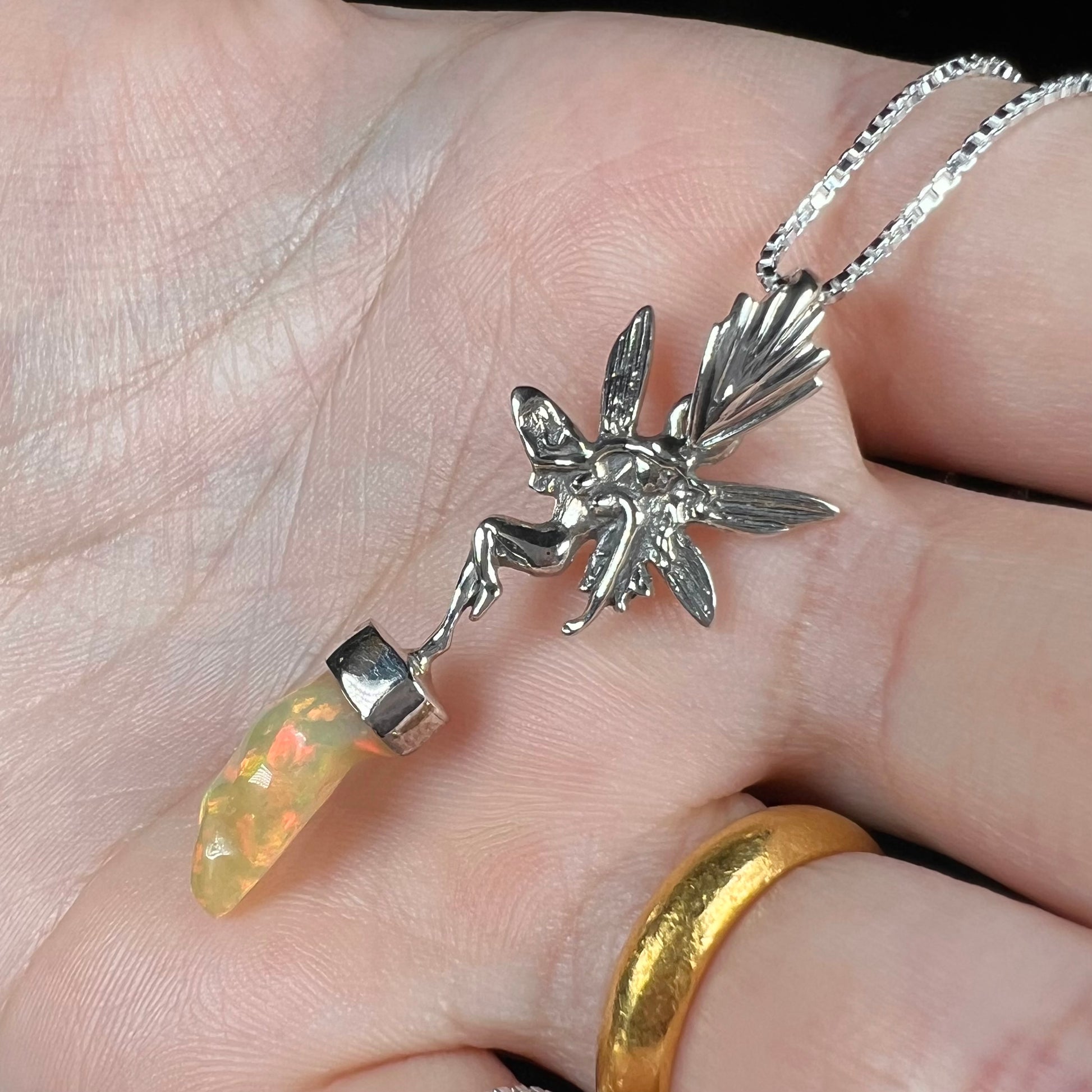 A sterling silver fairy necklace with an Ethiopian fire opal crystal, shown angled in a hand close-up.