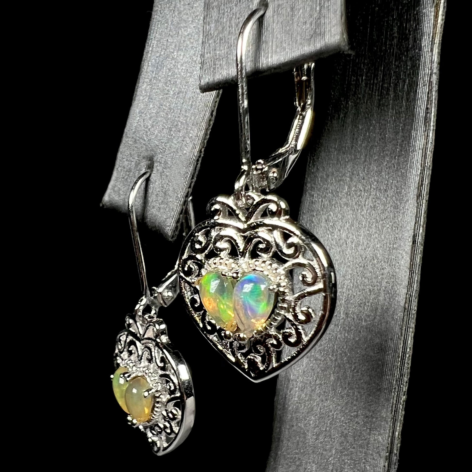 A pair of dangling sterling silver filigree heart earrings, each set with two Ethiopian opals.