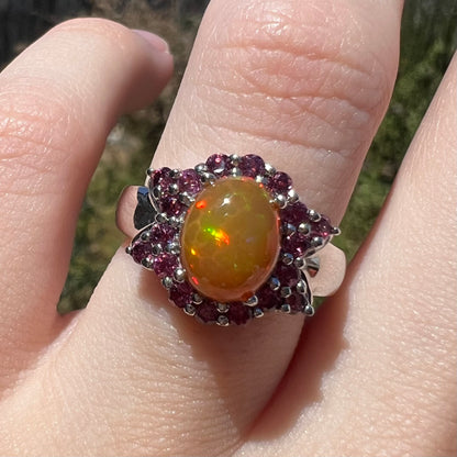Close-up sunlit view of silver Ethiopian opal ring with bowtie design garnet halo, worn on finger