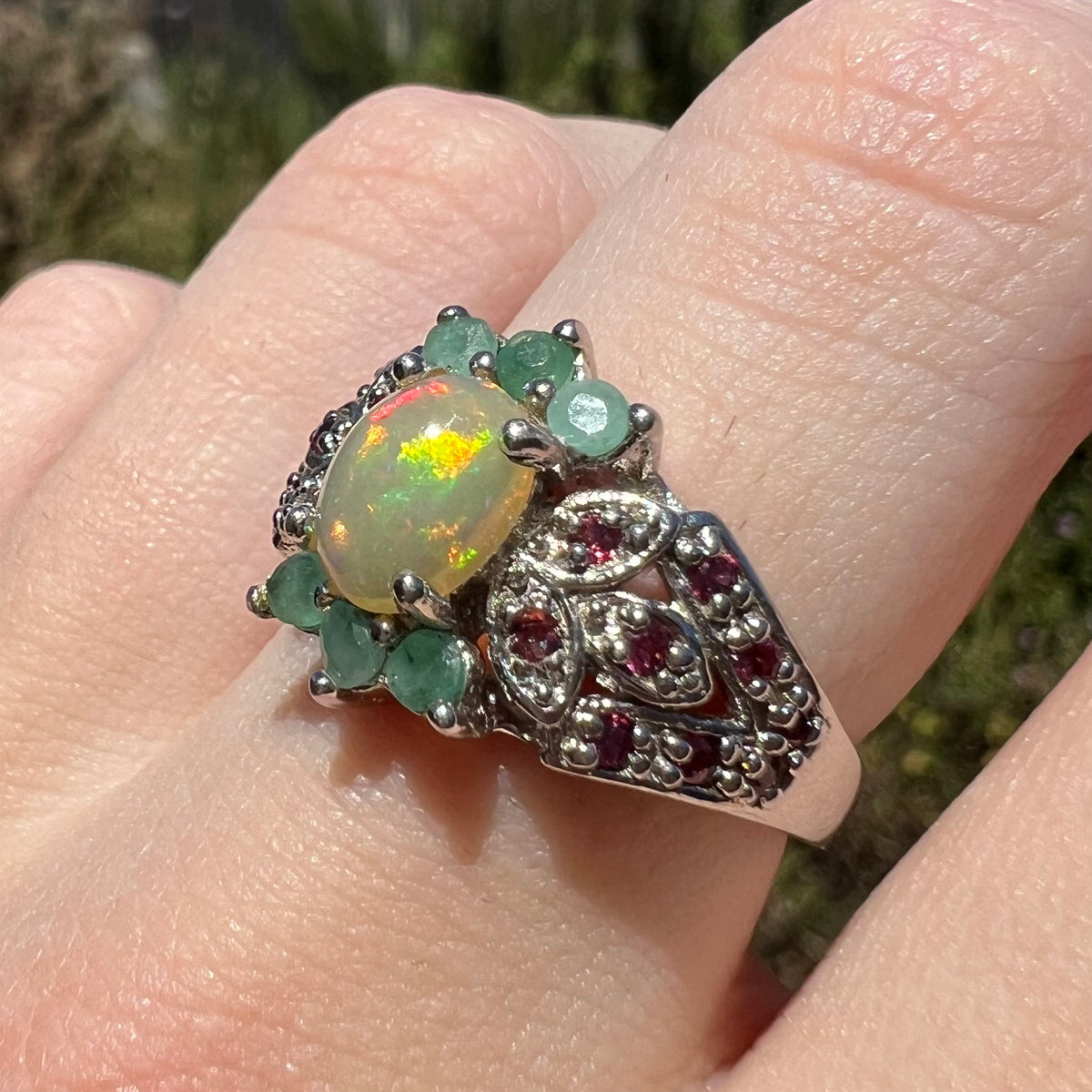 Angled close-up of Ethiopian opal, garnet, and green beryl ring, worn on finger in natural light