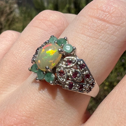 Angled close-up of Ethiopian opal, garnet, and green beryl ring, worn on finger in natural light