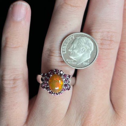 Close-up of hand wearing women's silver Ethiopian opal and garnet halo design ring next to US dime coin