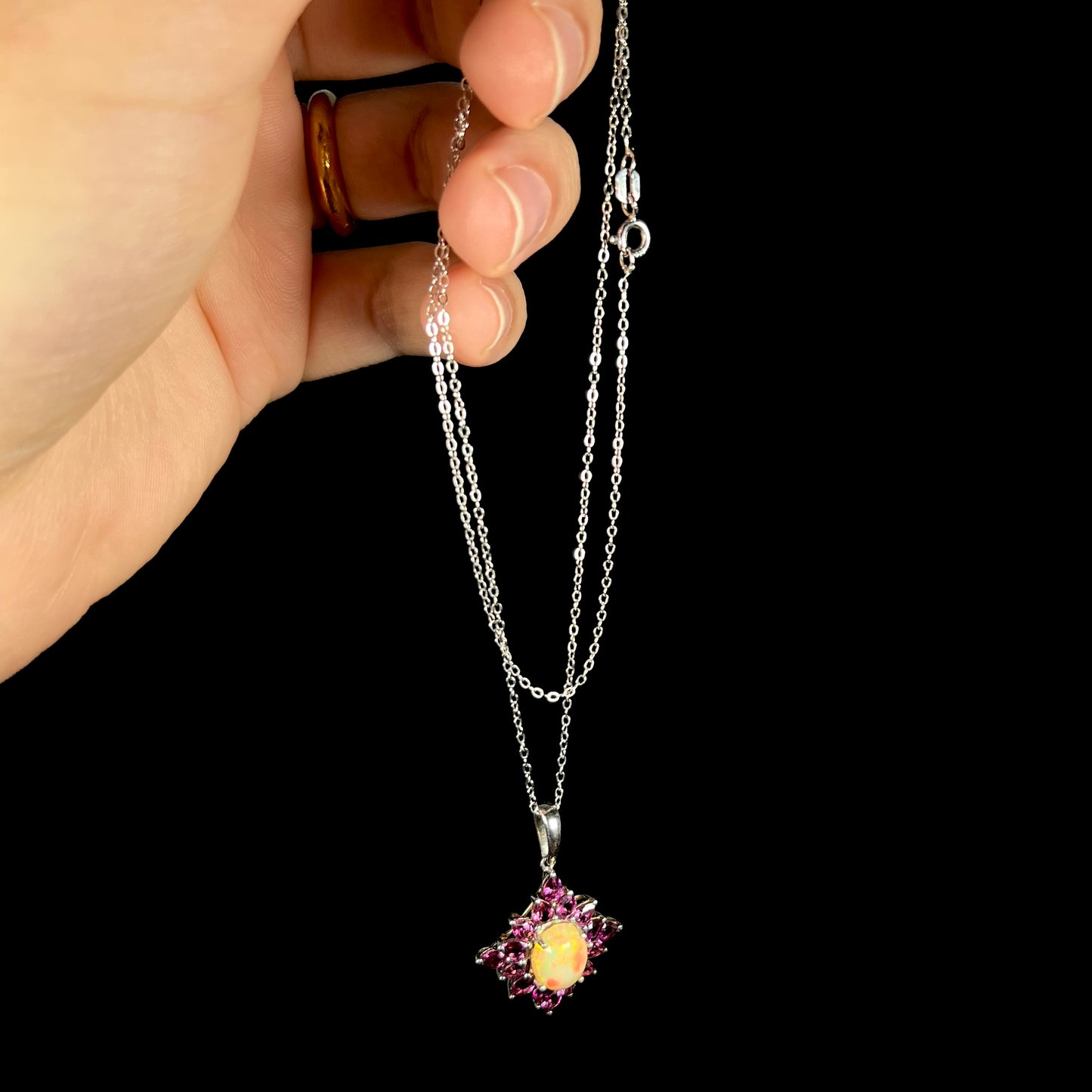 A sterling silver Ethiopian opal and rhodolite garnet spray necklace dangled from a hand by its chain.