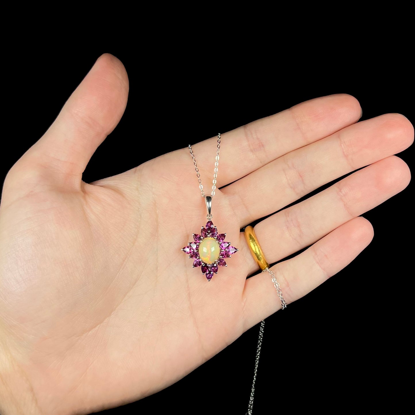 A sterling silver Ethiopian opal and rhodolite garnet spray necklace shown in a hand against a black background.