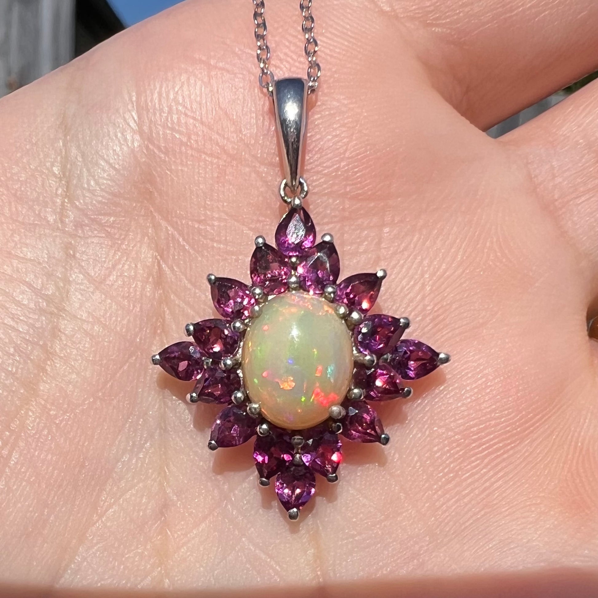 A sterling silver Ethiopian opal and rhodolite garnet spray necklace, shown close-up in sunlight, held in a hand.