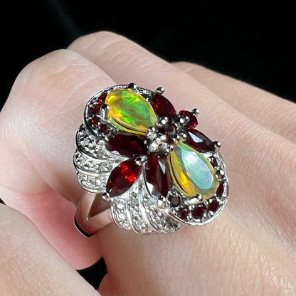 A sterling silver Ethiopian opal and garnet infinity-design ring with diamond accents, worn on a finger at an angle.