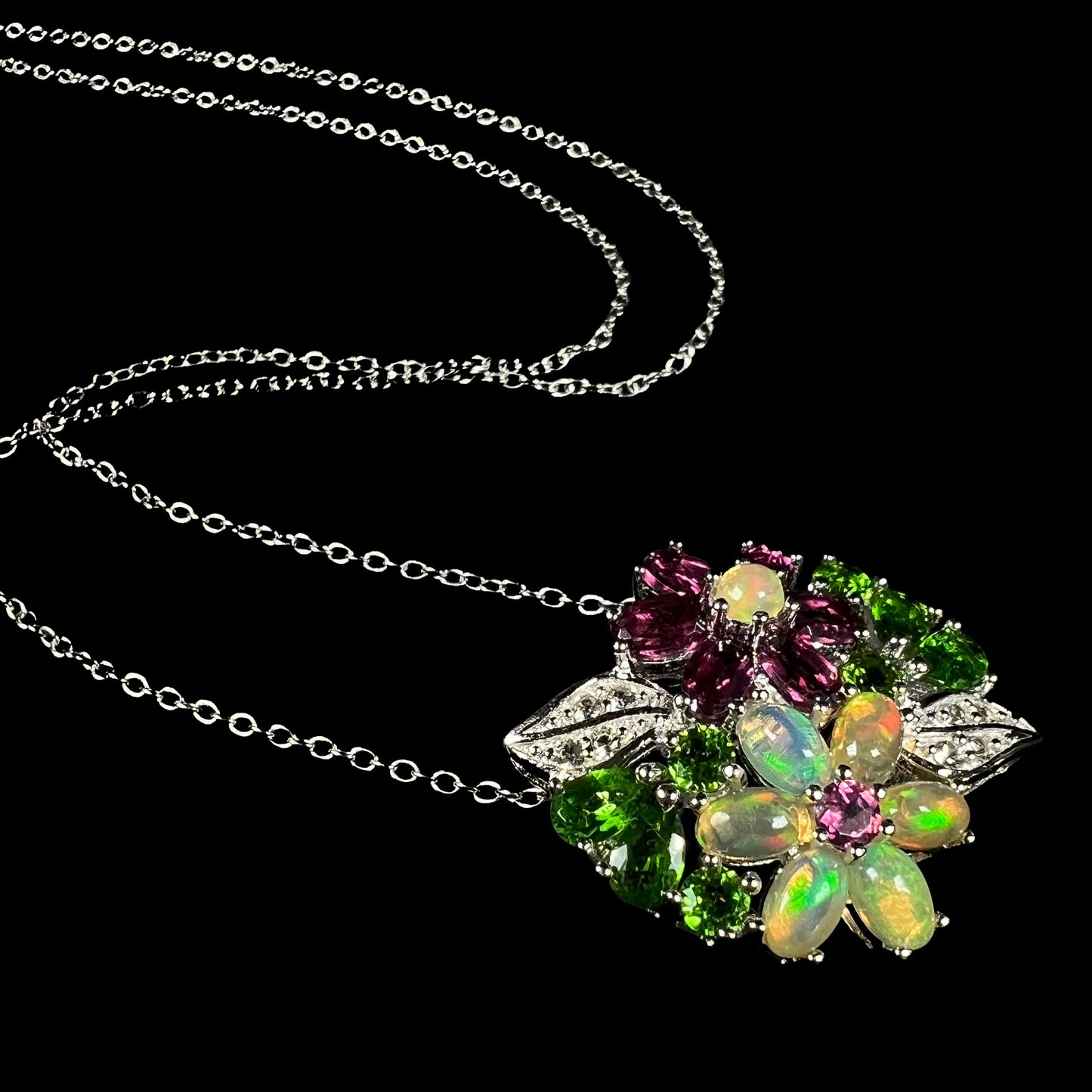 An Ethiopian opal and garnet gemstone flower necklace in silver, shown at an artistic angle against black background.