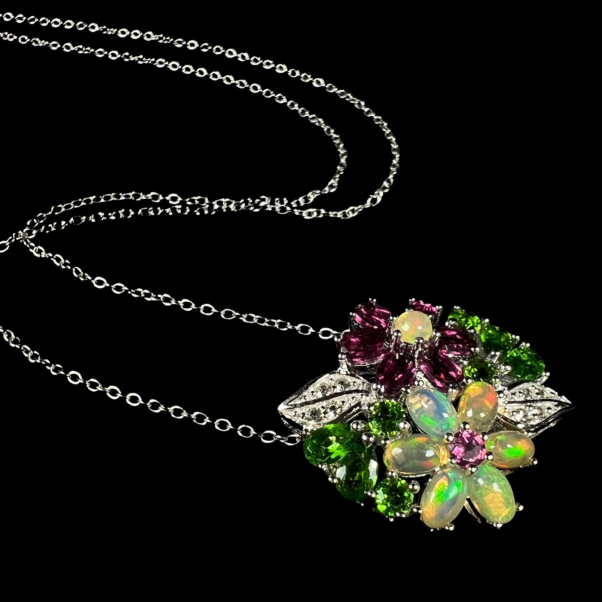 An Ethiopian opal and garnet gemstone flower necklace in silver, shown at an artistic angle against black background.