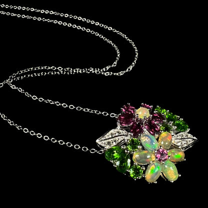 An Ethiopian opal and garnet gemstone flower necklace in silver, shown at an artistic angle against black background.