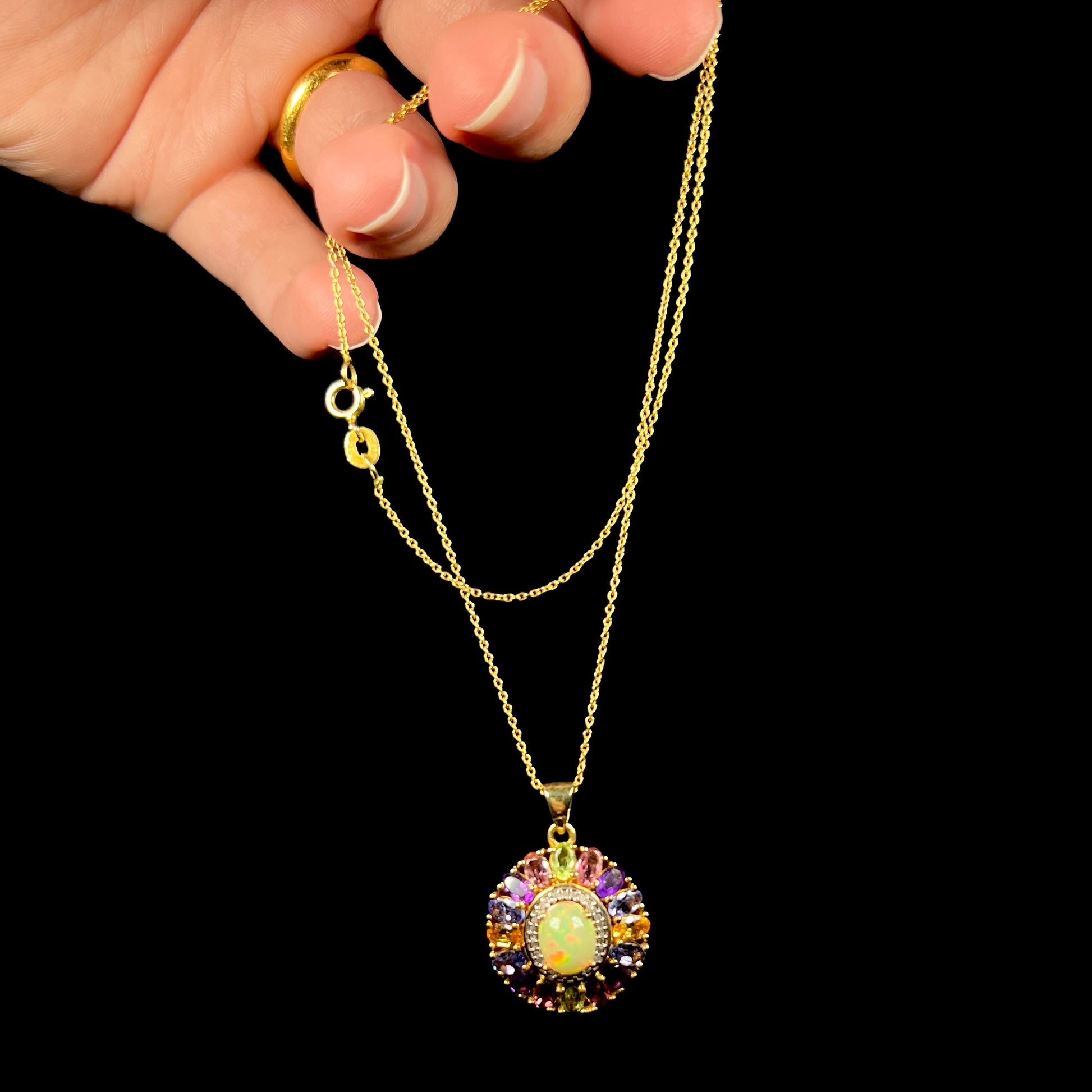 A gold plated sterling silver Ethiopian fire opal and multi-gemstone halo necklace dangled by its chain.