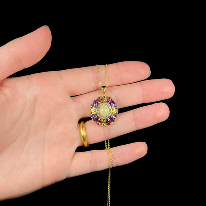 A gold plated sterling silver Ethiopian fire opal and multi-gemstone halo pendant shown in a hand.