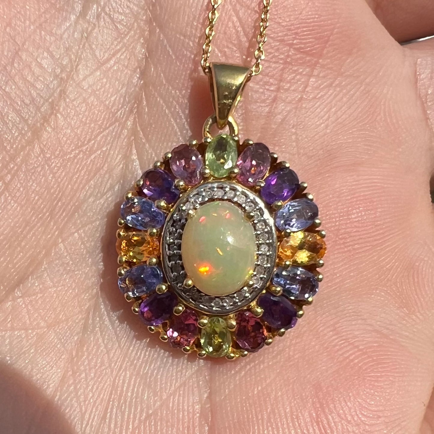 A gold plated sterling silver Ethiopian fire opal and multi-gemstone halo pendant shown close-up in sunlight.