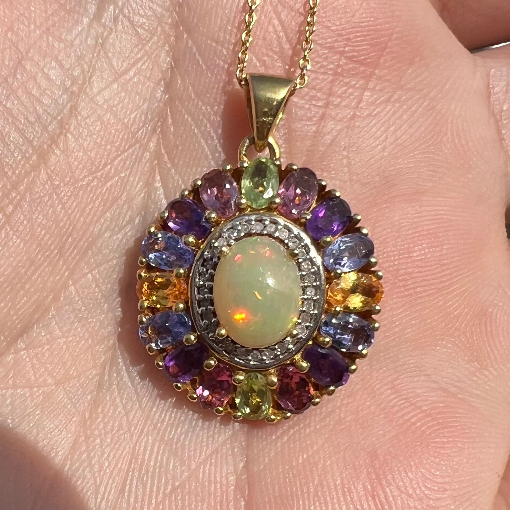 A gold plated sterling silver Ethiopian fire opal and multi-gemstone halo pendant shown close-up in sunlight.