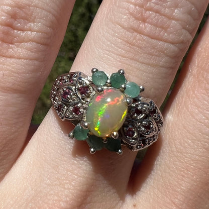 Close-up of sterling silver Ethiopian opal, green beryl, and garnet ring worn on finger in sunlight
