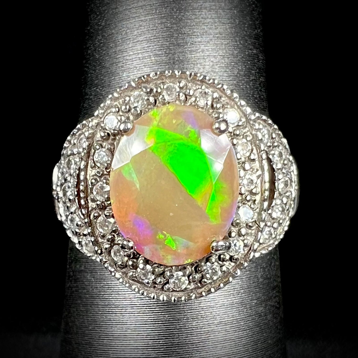 Front view of silver Ethiopian opal ring with CZ halo.  The faceted opal shows a diagonal bright green flash.