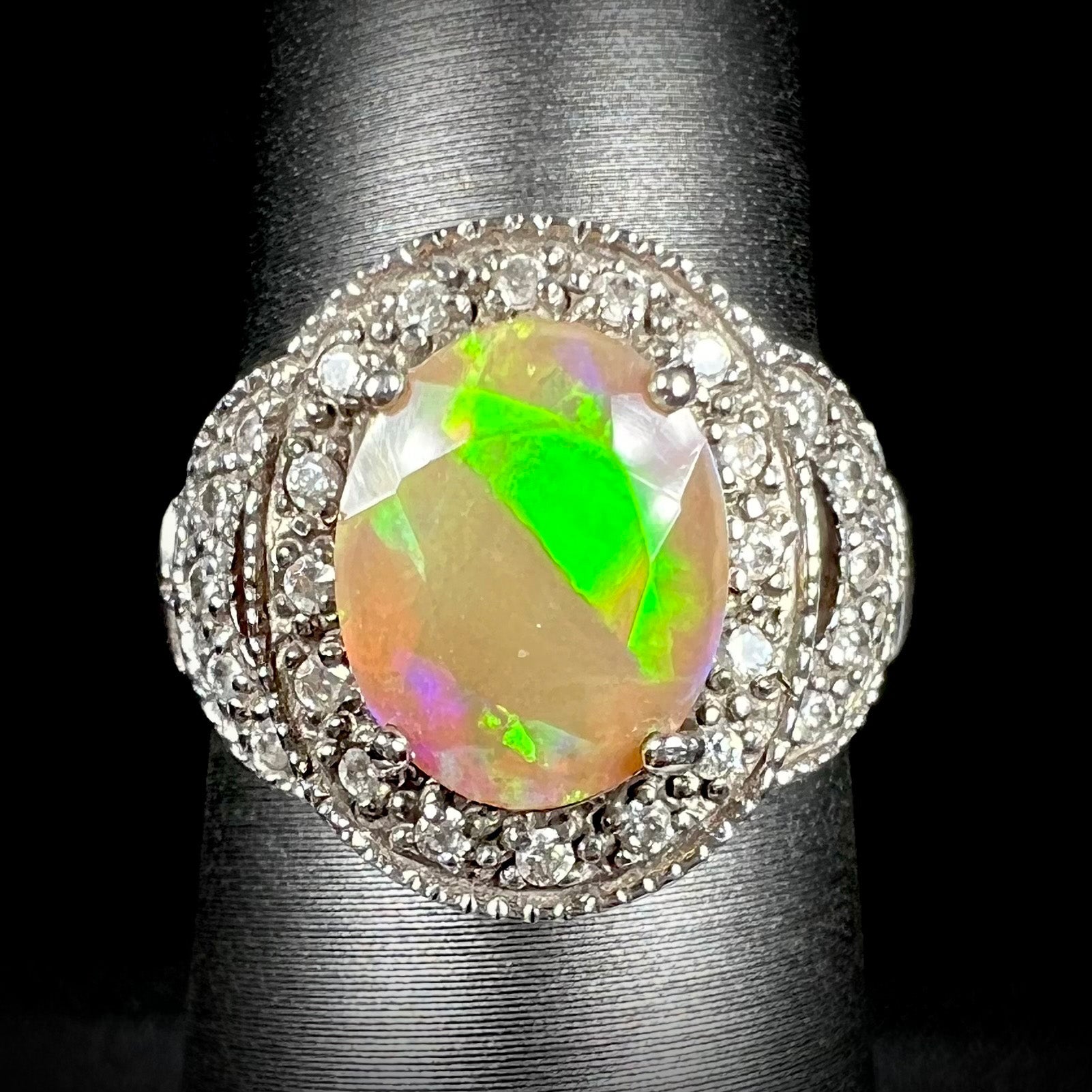 Front view of silver Ethiopian opal ring with CZ halo.  The faceted opal shows a diagonal bright green flash.