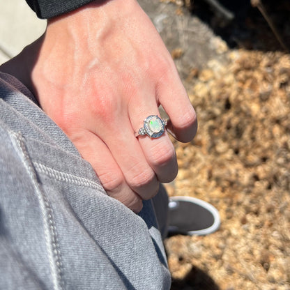 Person's hand resting on hip in sunlight wearing Ethiopian opal and CZ halo design ring