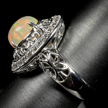 Side view of silver Ethiopian opal filigree halo ring against black background.