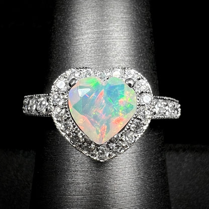 Close-up of heart shaped Ethiopian opal ring with CZ-set halo design and milgrain accents, shown on display