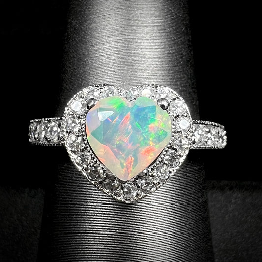 Close-up of heart shaped Ethiopian opal ring with CZ-set halo design and milgrain accents, shown on display