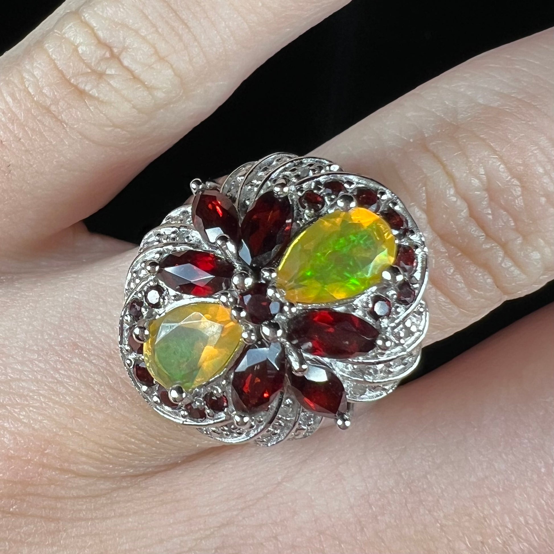 An Ethiopian opal infinity ring with garnet and diamond accents, worn on a finger.