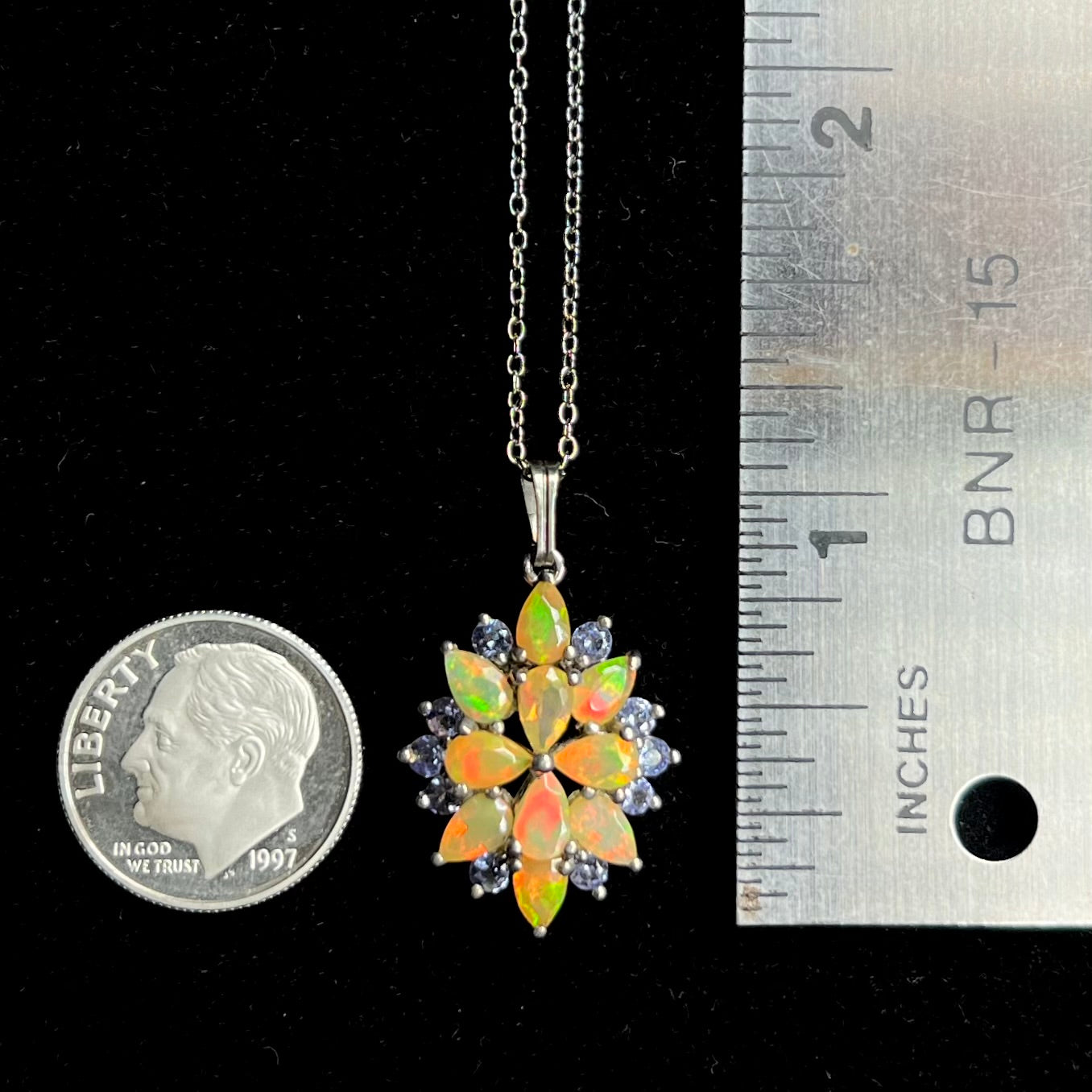 An Ethiopian opal cluster necklace that measures 1.25 inches long, resting next to a dime coin and ruler.