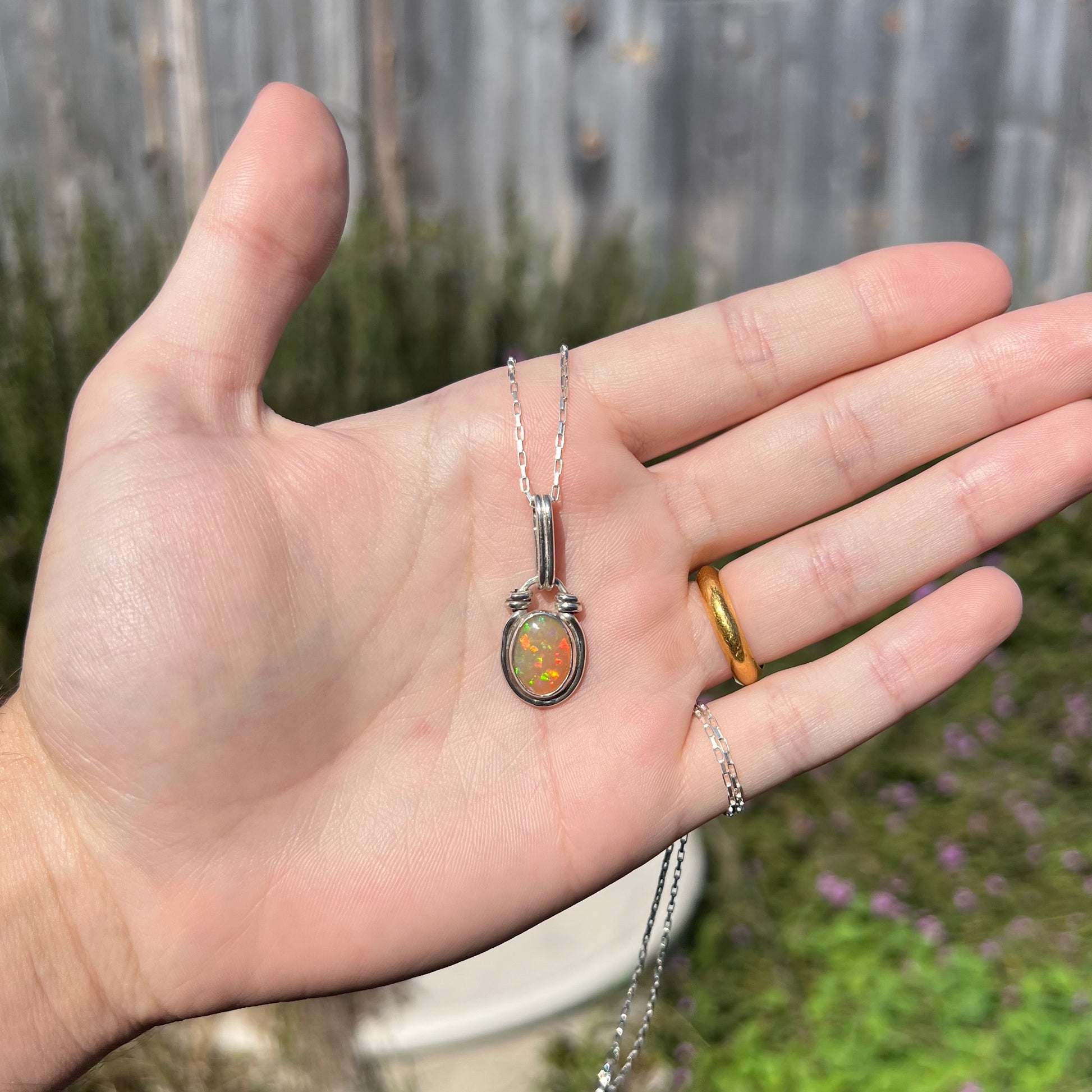 A colorful sterling silver Ethiopian opal necklace shown in a hand in an outdoor, sunlit environment.