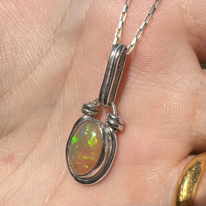 A colorful sterling silver Ethiopian opal pendant shown close-up from an angle in the sunlight against a hand.