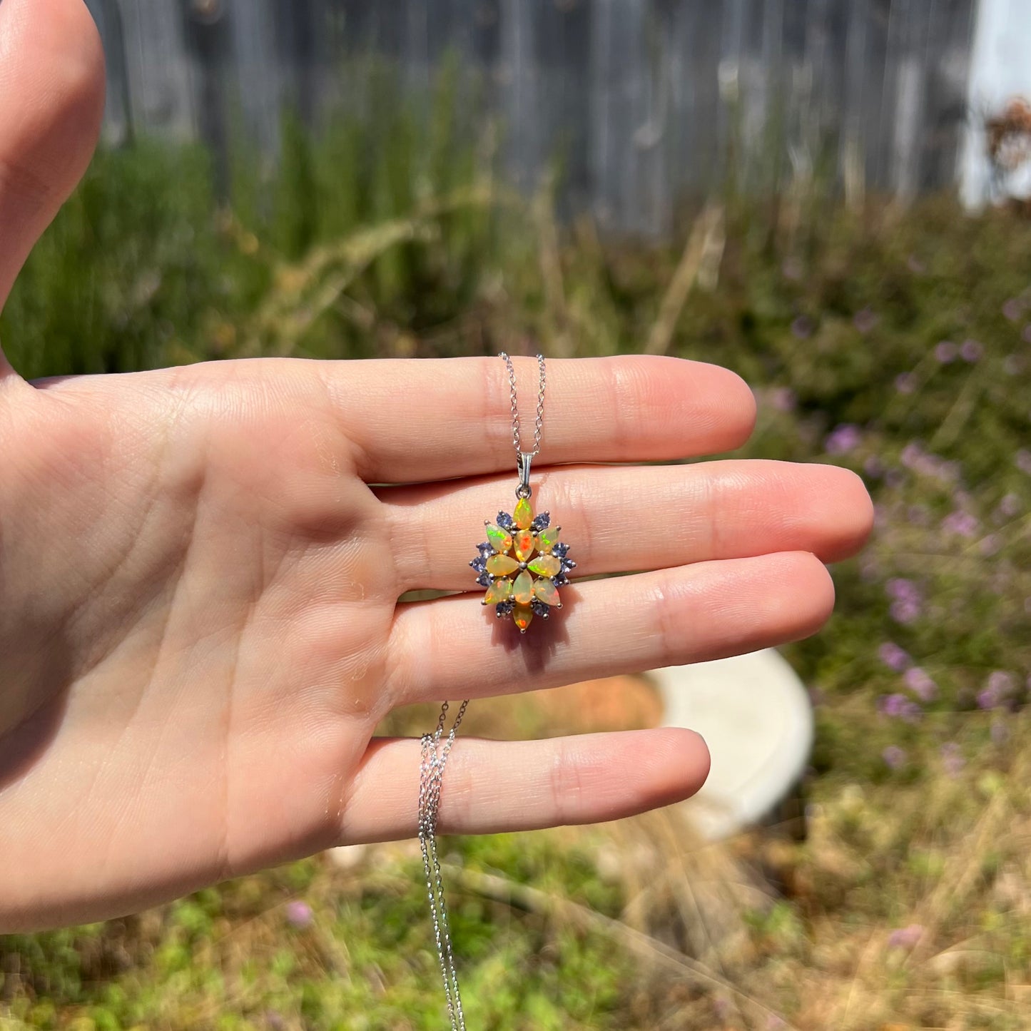 A brightly colored Ethiopian opal necklace held in a hand at a distance in the sunlight.