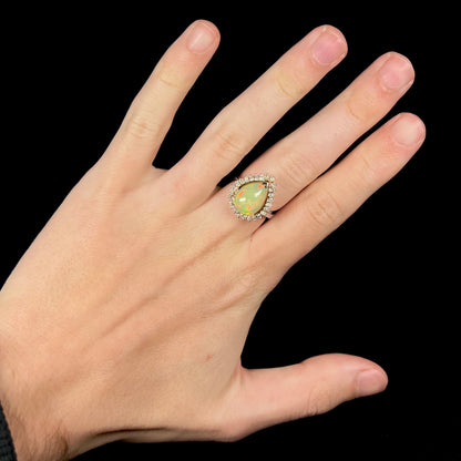 Hand wearing a pear shaped Ethiopian opal and diamond halo engagement ring on middle finger.