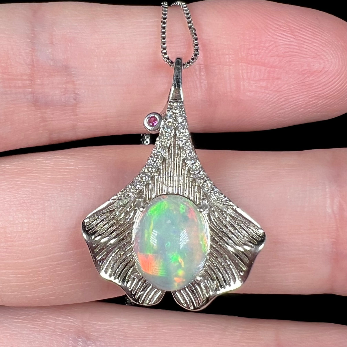 Close-up of Ethiopian opal and pink sapphire-accented pendant with sterling silver ginko leaf motif, held in hand