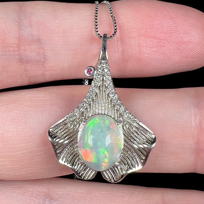 Close-up of Ethiopian opal and pink sapphire-accented pendant with sterling silver ginko leaf motif, held in hand
