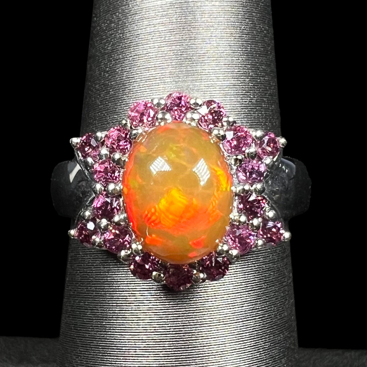 Close-up of dark honey-colored Ethiopian opal and purple rhodolite garnet ring in sterling silver with bowtie halo design, shown on ring display