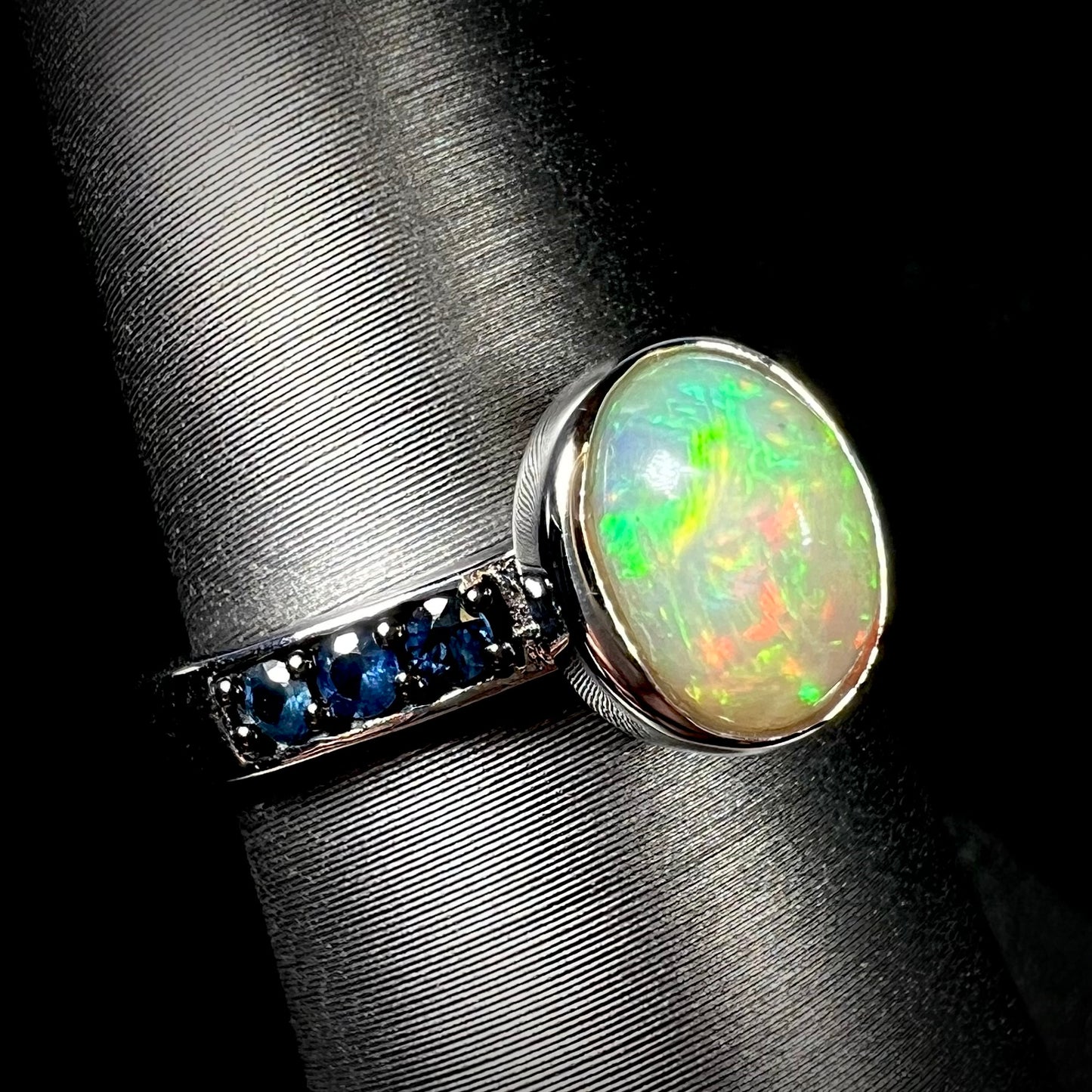 Angled view of Ethiopian opal ring in sterling silver with topaz accents against black background.