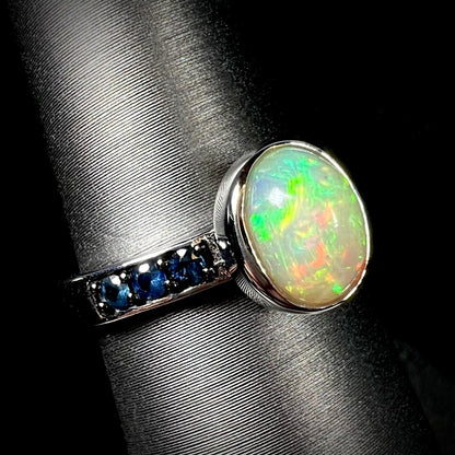 Angled view of Ethiopian opal ring in sterling silver with topaz accents against black background.