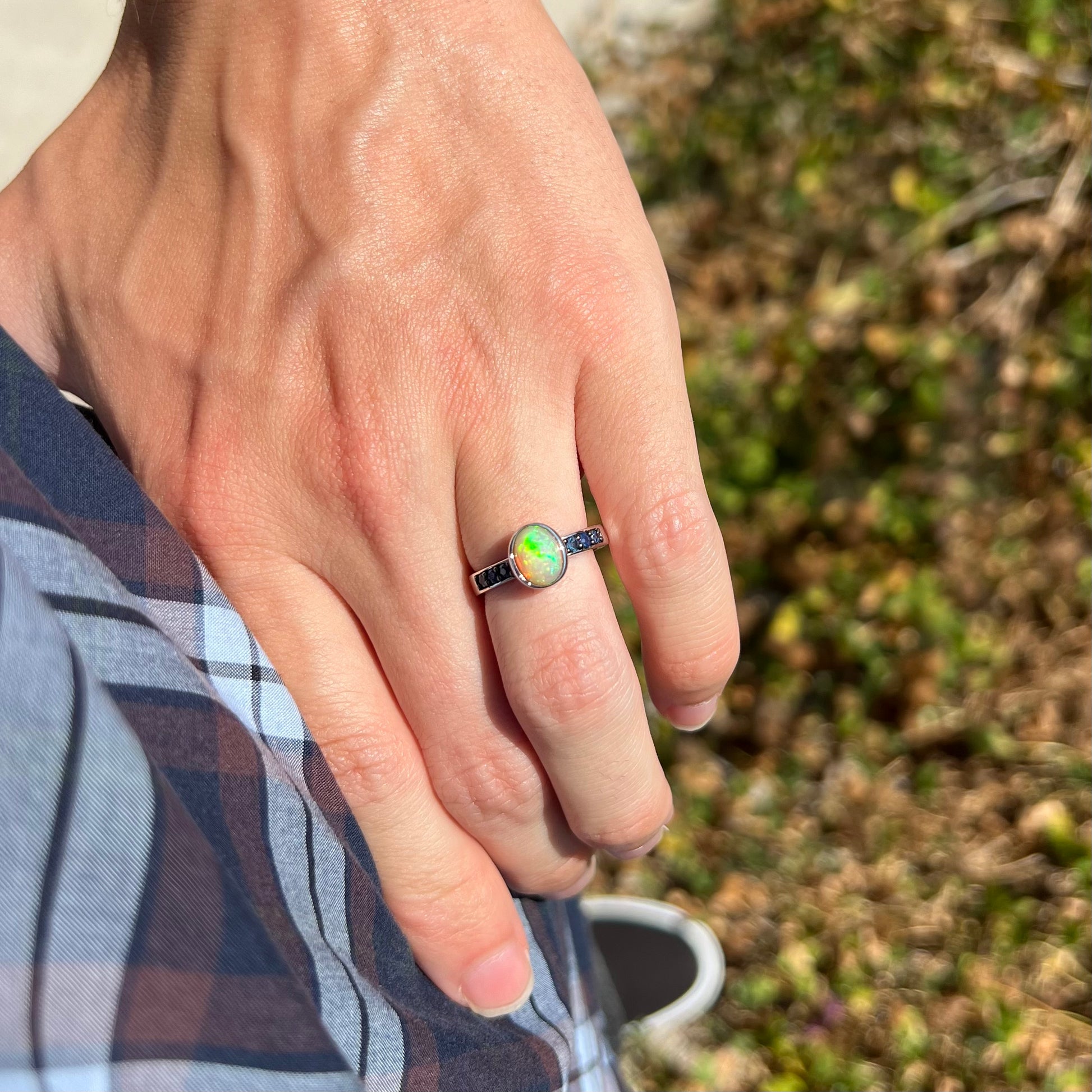 Hand wearing Ethiopian opal ring on their hand in the sunlight, with their hand on their hip.